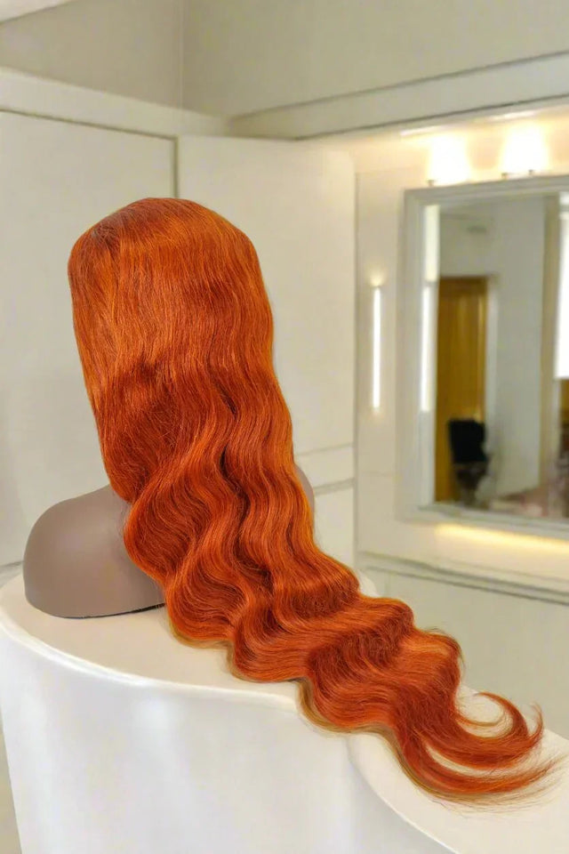 Vibrant orange human hair wig with loose waves displayed on mannequin in modern salon setting