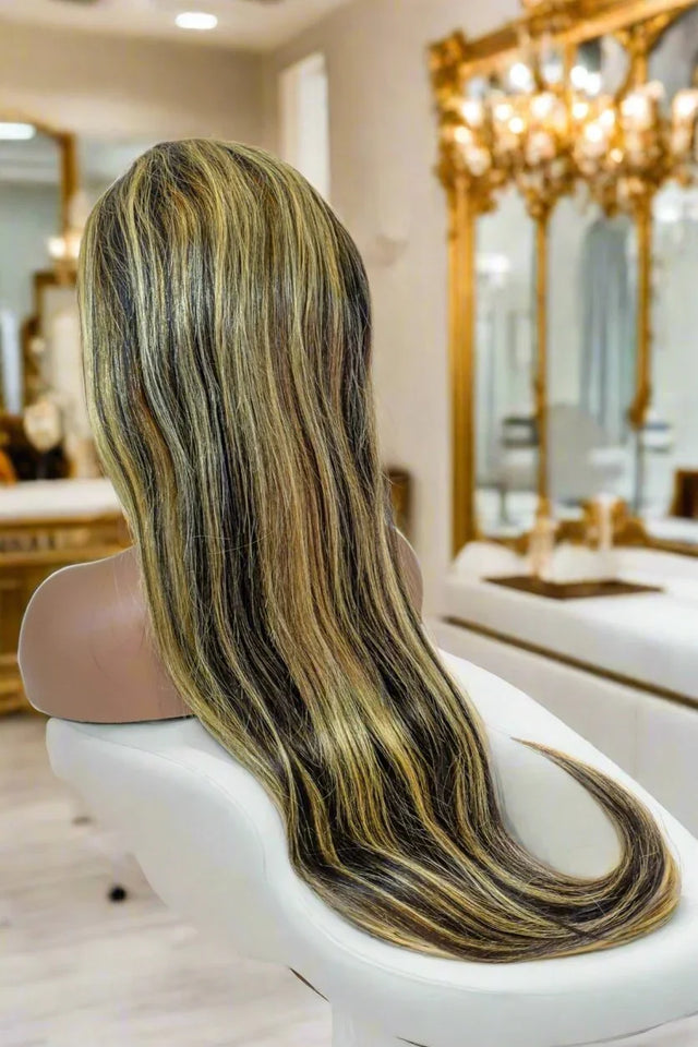 Long human hair wig with dark roots and golden blonde highlights, styled on mannequin in luxury salon setting