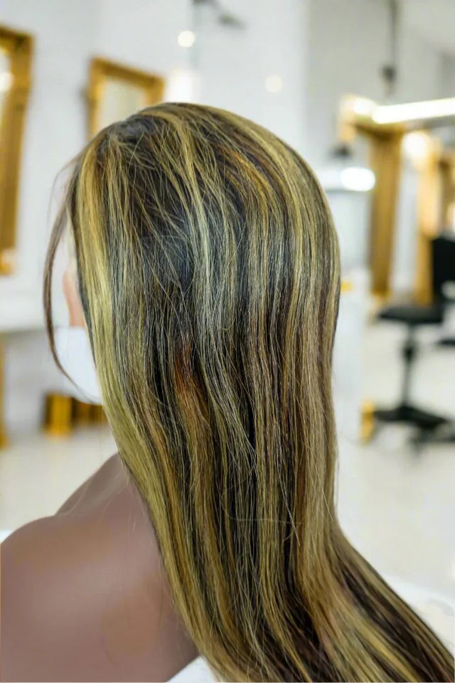 Long human hair wig with dark roots and golden blonde highlights, styled in a salon setting