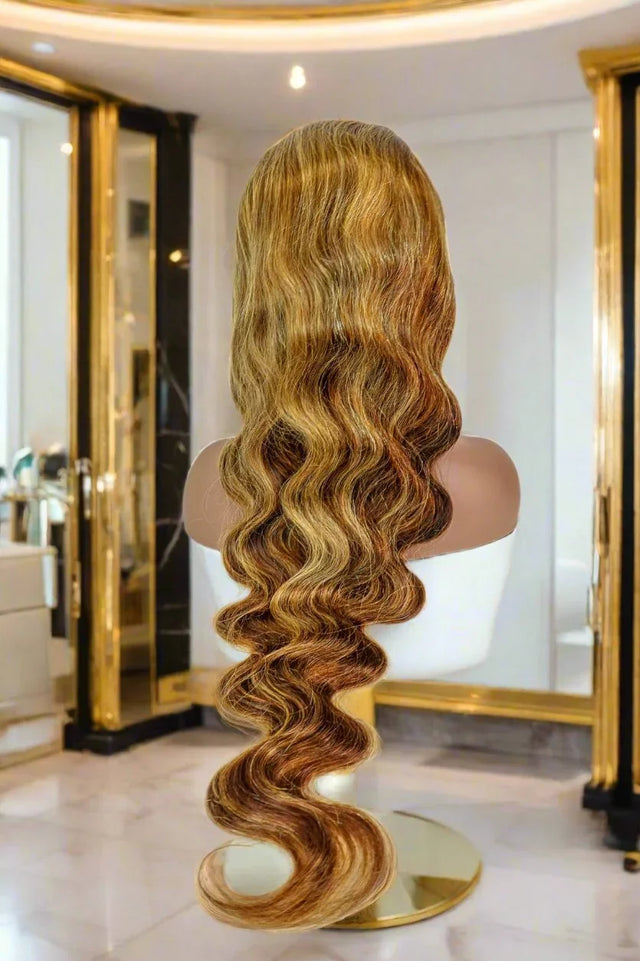 Long human hair wig with body waves, golden brown ombre, displayed on mannequin in luxury salon setting