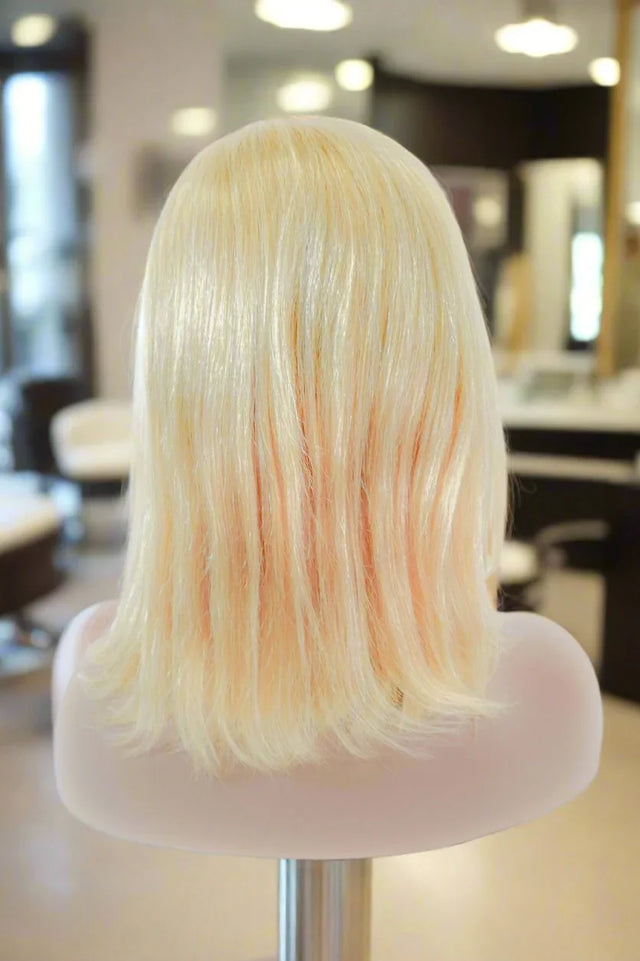 Blonde human hair wig with subtle peach highlights, styled on mannequin in salon setting