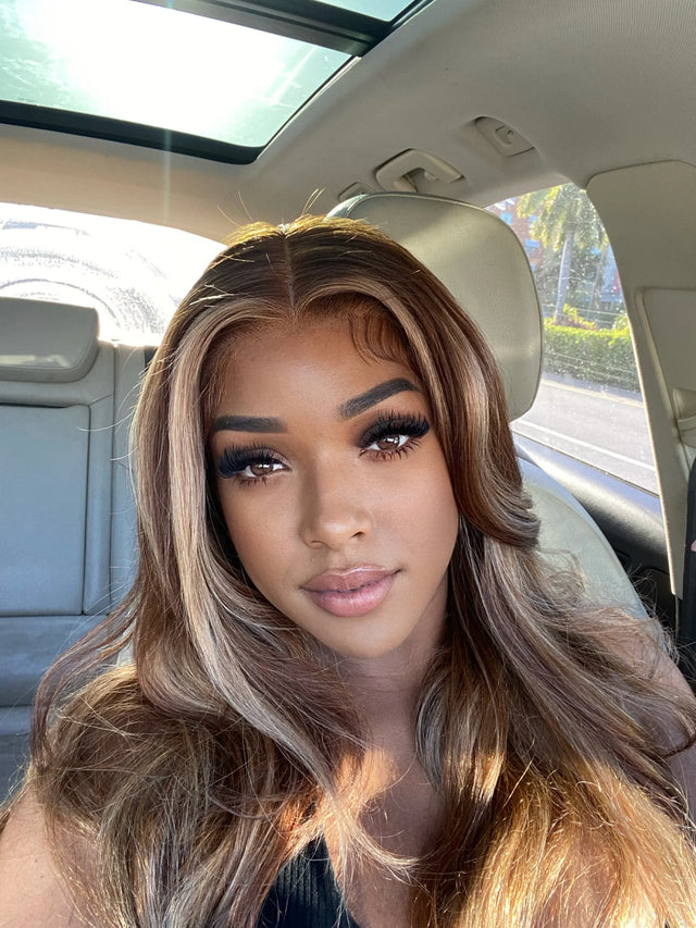 Woman wearing a natural-looking human hair wig with highlights, seated in a car with sunroof open
