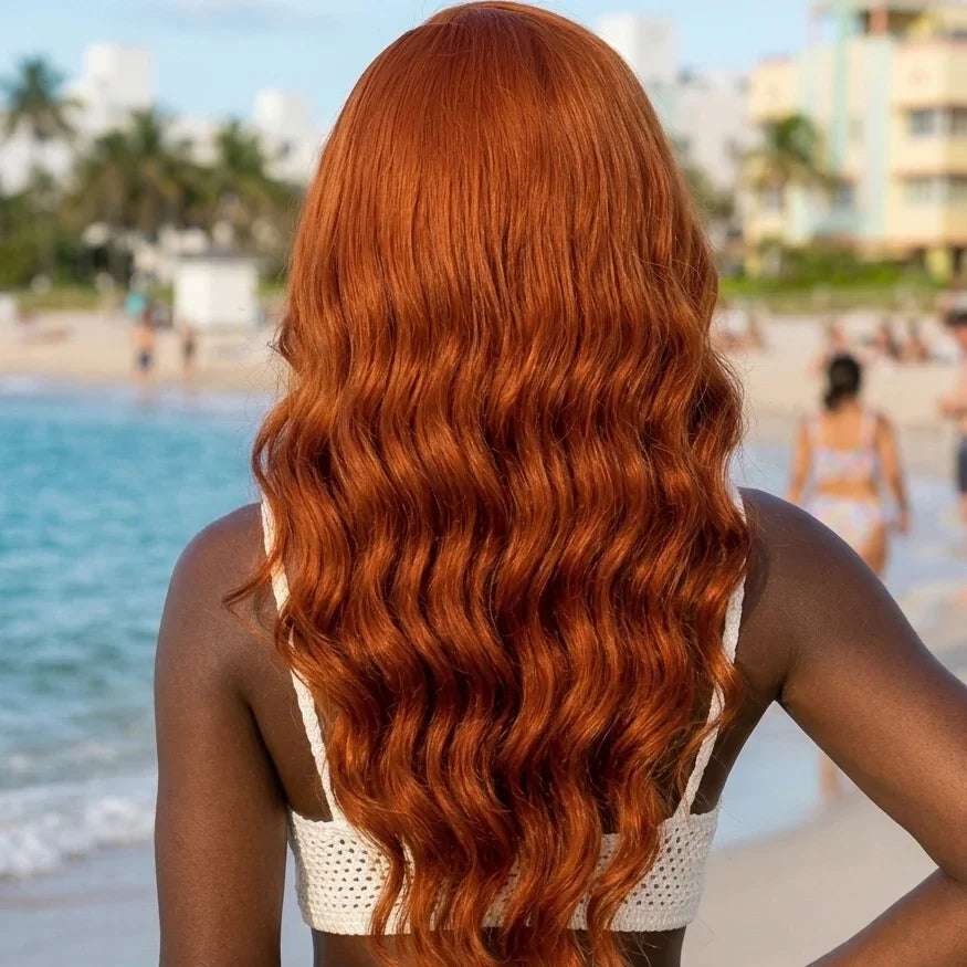 Woman with long, wavy orange ginger hair on a beach with ocean and buildings in the background