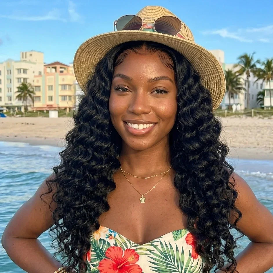 Woman with long curly human hair wig at beach, wearing straw hat and floral top
