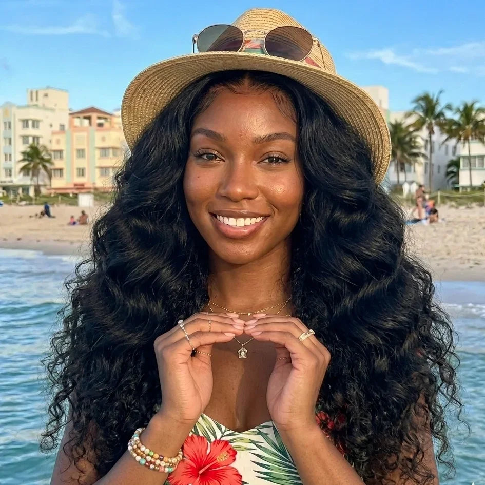 Woman with long curly human hair wig at beach, wearing straw hat and floral top