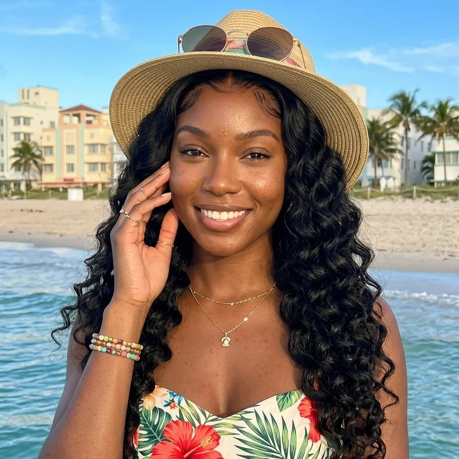 Woman with long curly human hair wig at beach, wearing straw hat and floral top