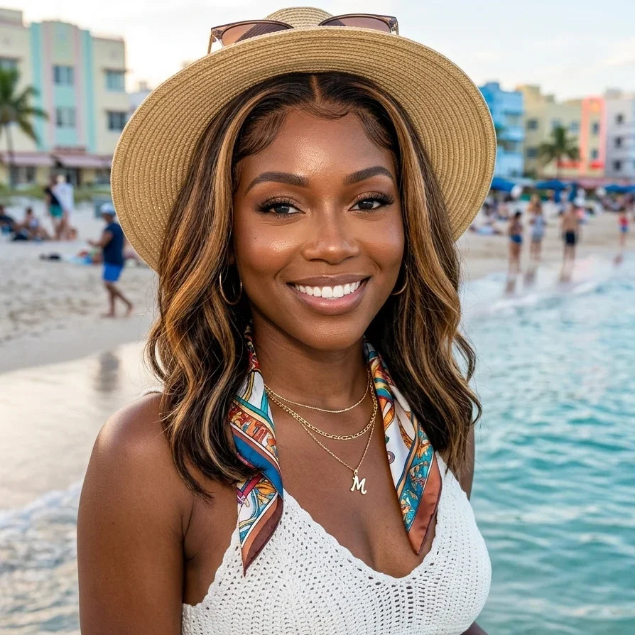 Woman with wavy human hair wig smiling at beach, wearing straw hat and white top