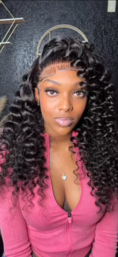 Woman wearing curly human hair wig with lace front, styled in voluminous curls, paired with pink top.