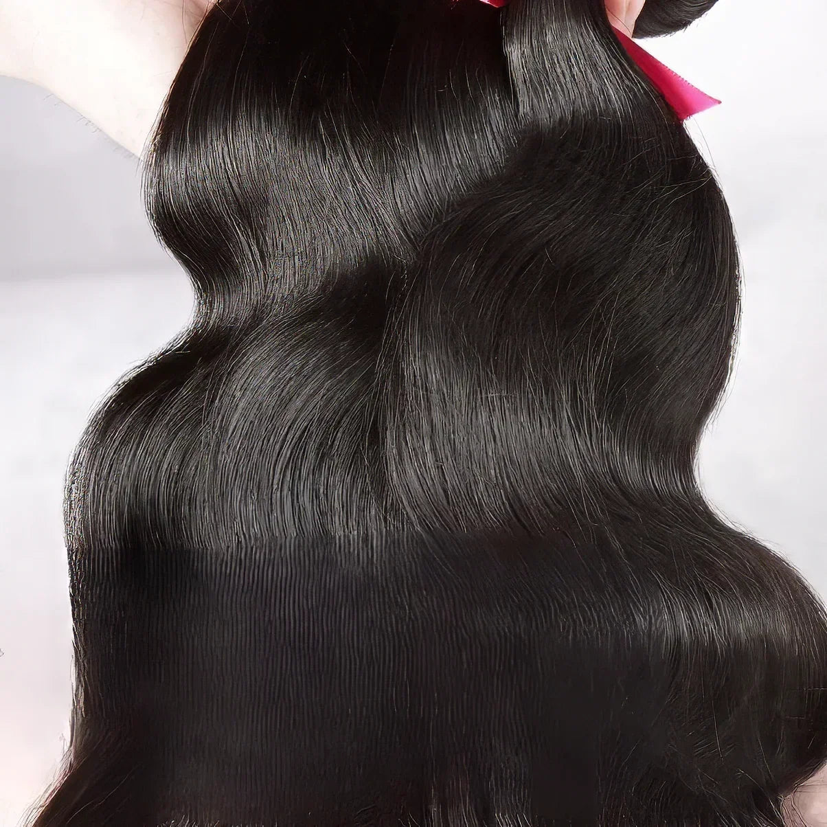 Luxury human hair bundles with natural body wave texture, sleek black color, and pink ribbon tie