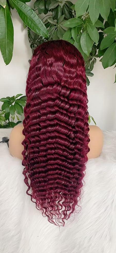 Deep burgundy human hair wig with voluminous body waves, displayed on mannequin against green foliage