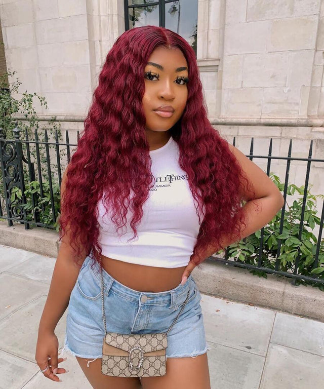 Woman wearing long, curly burgundy human hair wig, styled for natural look with casual summer outfit
