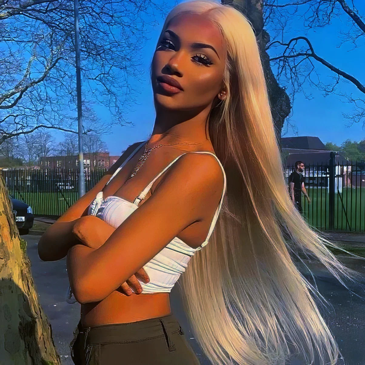 Woman with long blonde human hair wig, styled straight, outdoors near tree