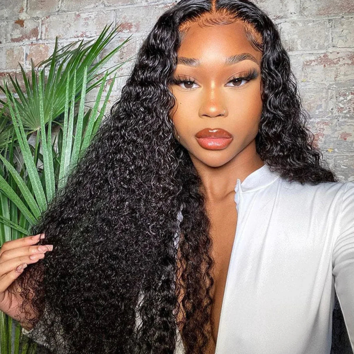 Woman with long, wavy hair wearing a white top against a brick wall background.