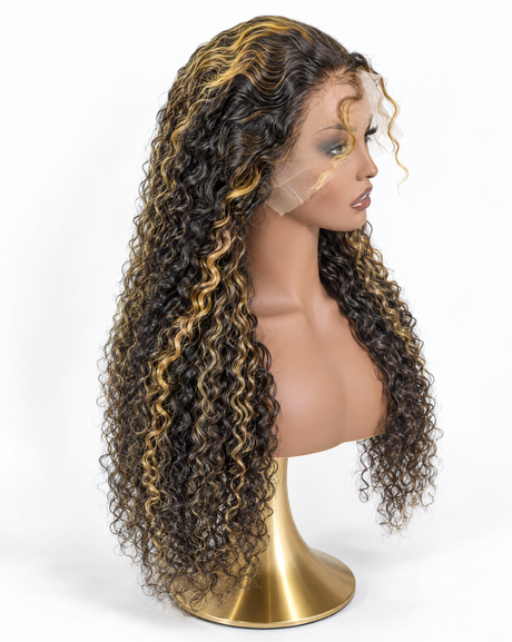 A long, curly wig displayed on a mannequin bust with a gold stand against a plain white background. The wig has dark brown to black curls with prominent golden blonde highlights throughout.