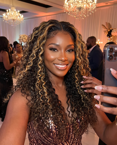 A woman taking a selfie in a formal event hall, showcasing a long, wavy, curly wig with dark brown and golden blonde highlights. She is wearing Bohemian 15A Transparent 13x4 Full Frontal 180 Density Natural Black & Blonde 27