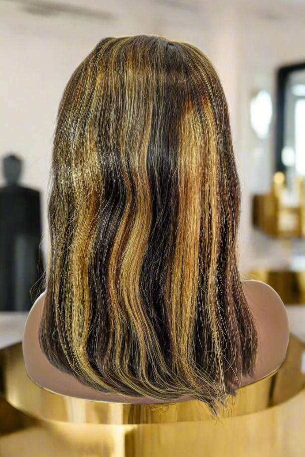 Human hair wig with dark roots and golden highlights, styled in loose waves on mannequin head