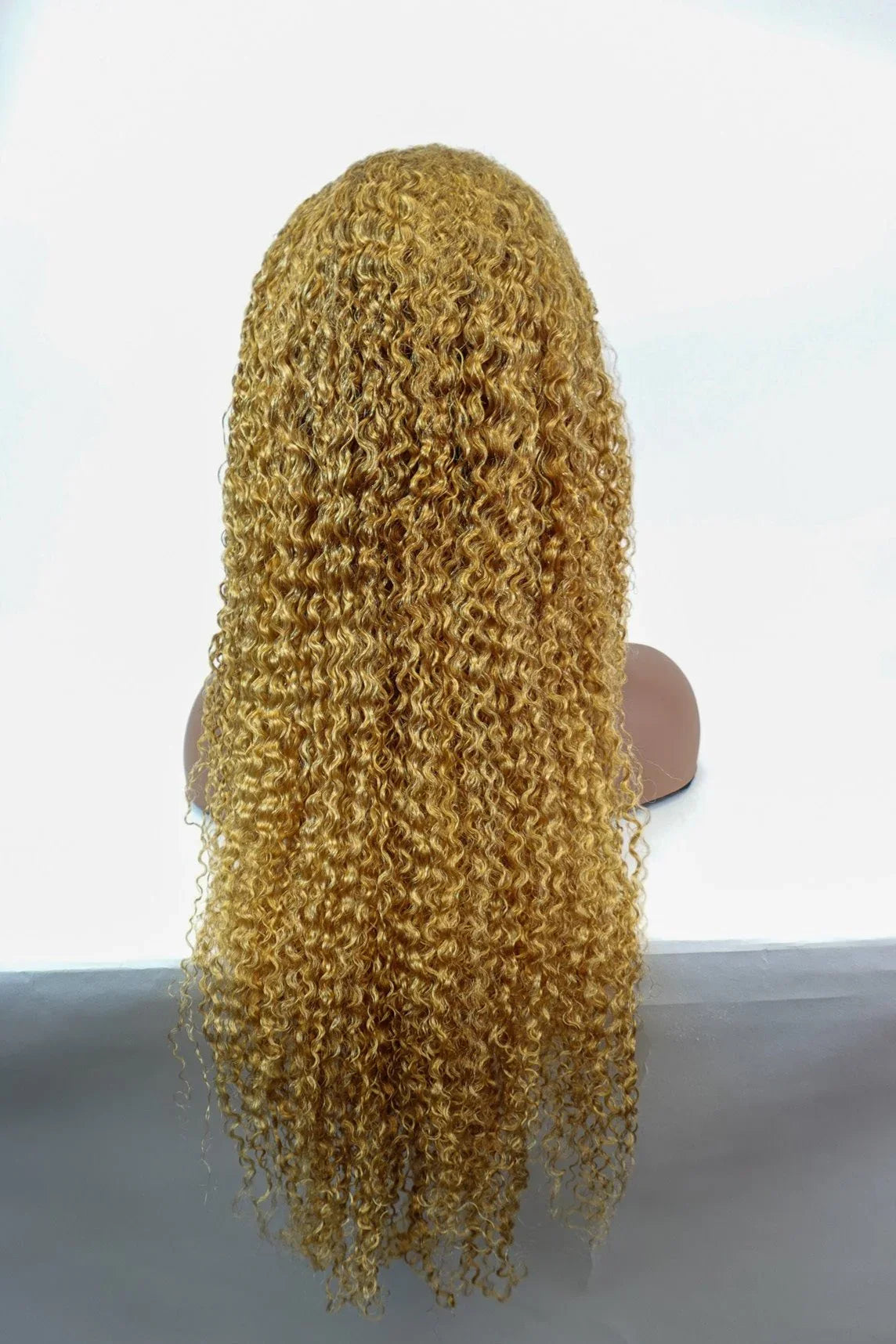 Golden curly human hair wig with voluminous waves, displayed on mannequin for natural styling