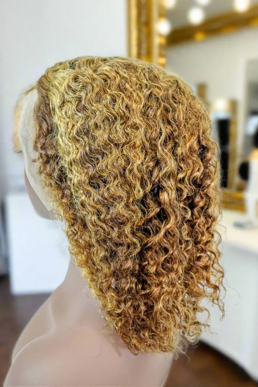 Curly human hair wig with honey blonde highlights on mannequin, salon mirror background