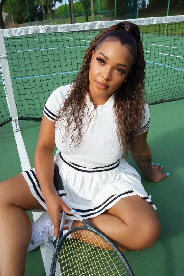 Woman with curly human hair wig in tennis outfit on court, holding racket