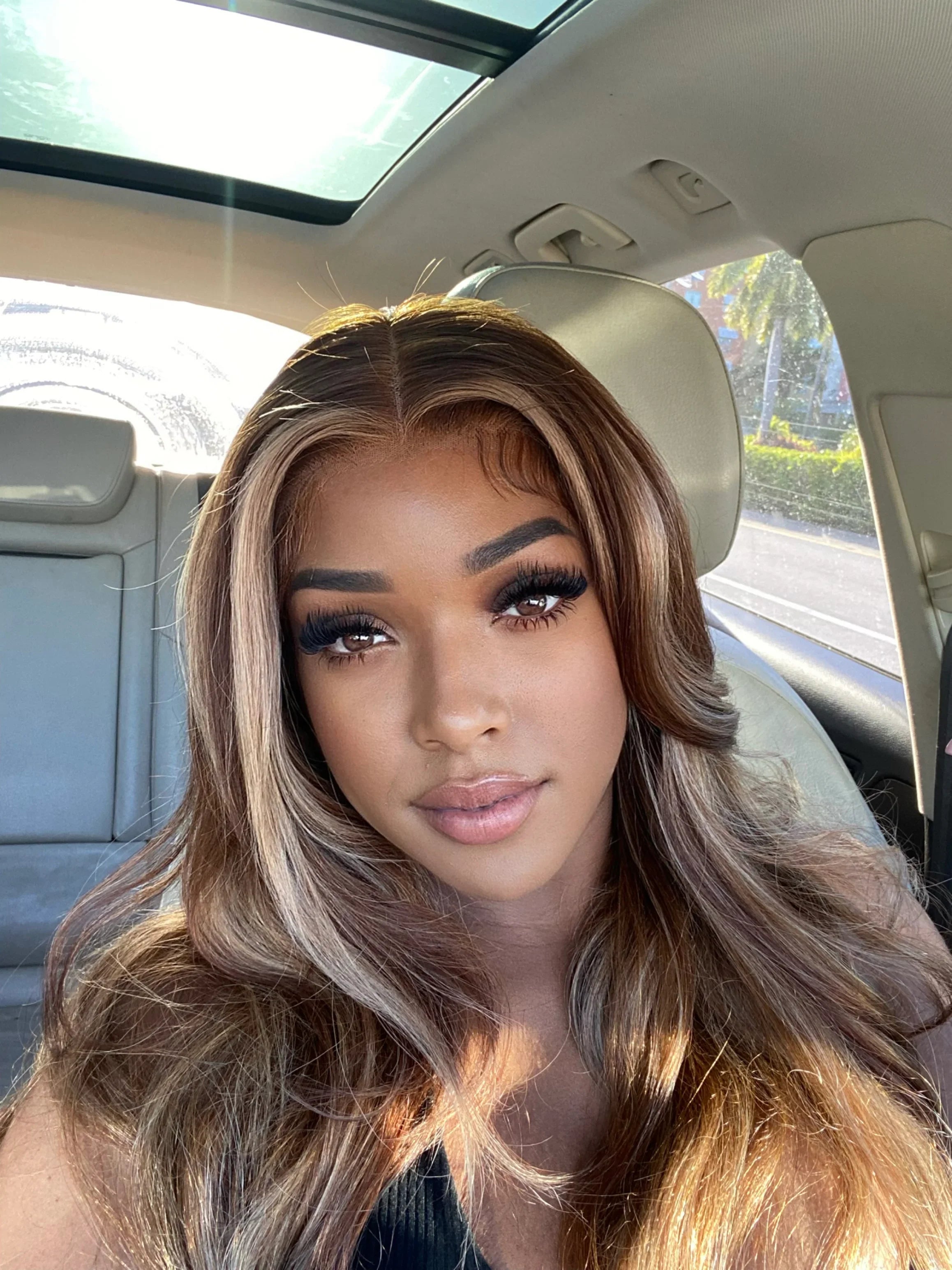 Woman wearing a natural-looking human hair wig with highlights, seated in a car with sunroof open